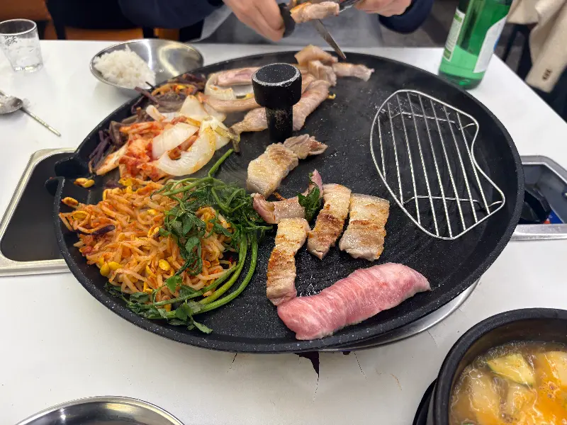 솥뚜껑에 구운 삼겹살과 다양한 채소들, 그리고 한강 라면