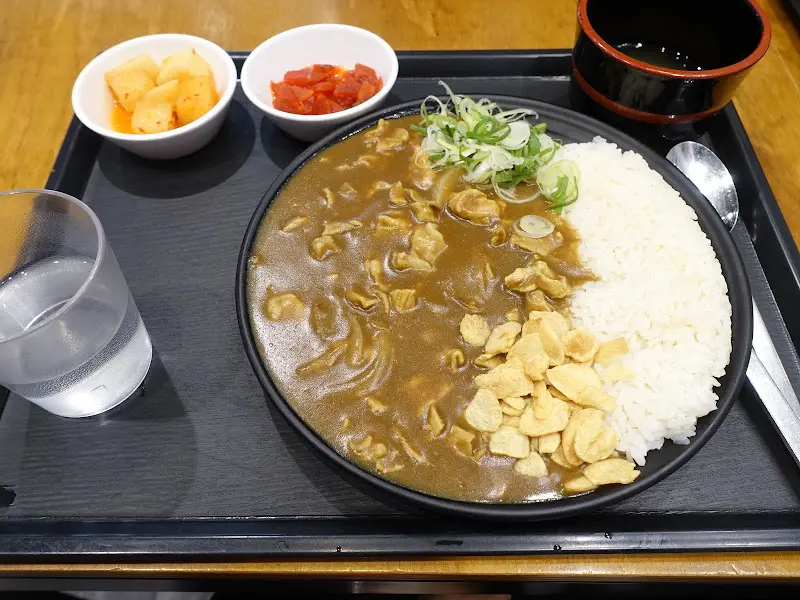 카레라이스, 깍두기, 단무지가 검은색 트레이에 담겨 테이블 위에 놓여 있다.