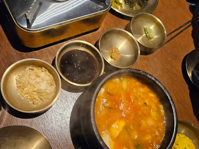 뜨거운 김이 올라오는 순두부찌개와 여러 가지 소스가 담긴 놋그릇들