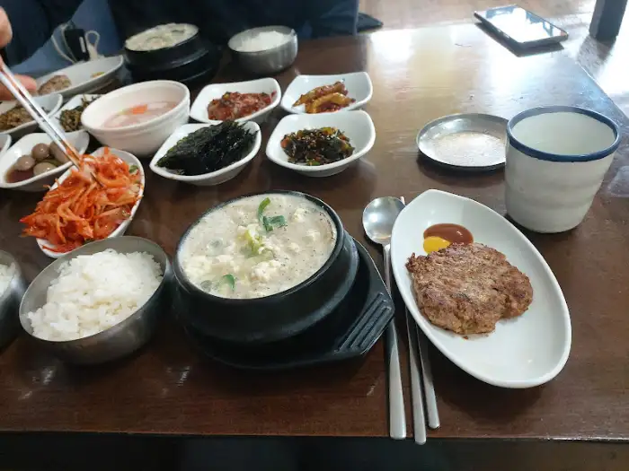 식탁 위에 놓인 밥, 순두부찌개, 두부 스테이크, 그리고 여러 반찬들