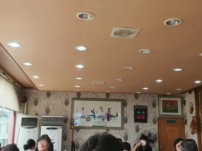 식당 내부의 천장 모습. 여러 개의 원형 조명이 켜져 있고, 환풍구와 그림 액자가 걸려 있다. 옅은 베이지색 벽과 어우러져 아늑한 분위기를 자아낸다.