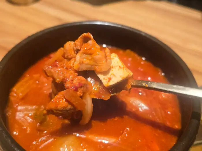 한국식 뚝배기에 담긴 김치찌개의 일부가 숟가락에 떠져 있습니다.
