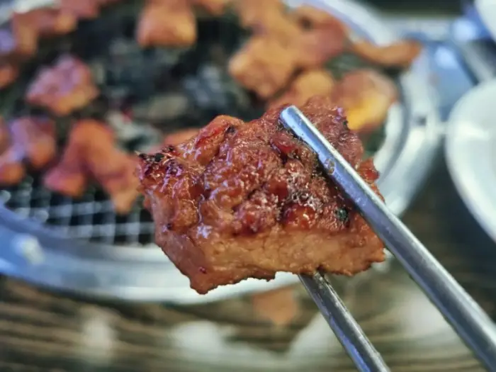 집게로 집어 올린 잘 구워진 갈매기살 조각