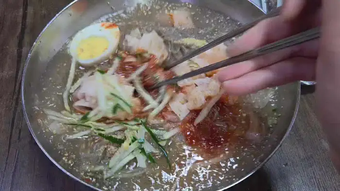 젓가락으로 냉면을 집어 올리는 모습, 풍성한 면발과 고명이 돋보인다.