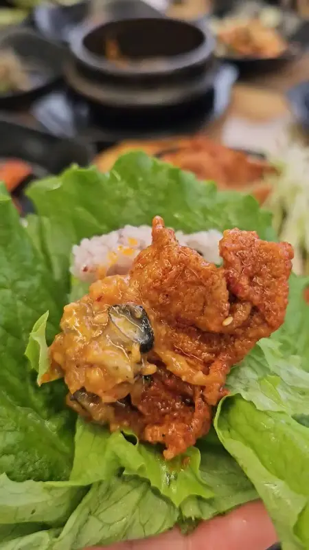 쌈 채소에 제육볶음, 쌈장, 우렁된장을 올려 쌈을 싸 먹는 모습