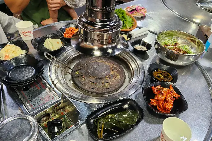 고기 굽는 모습. 잘 익은 고기를 뒤집으며 숯불의 열기가 느껴지는 듯합니다. 곁들임으로 나온 마늘도 함께 구워지고 있습니다.
