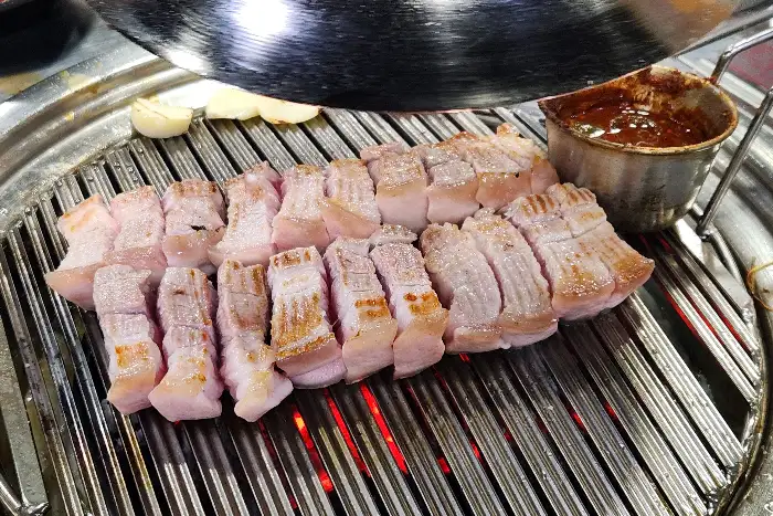잘 구워진 삼겹살 조각들이 불판 위에서 더욱 먹음직스럽게 보입니다. 붉은 숯불과 조화롭게 어우러져 따뜻한 느낌을 줍니다.