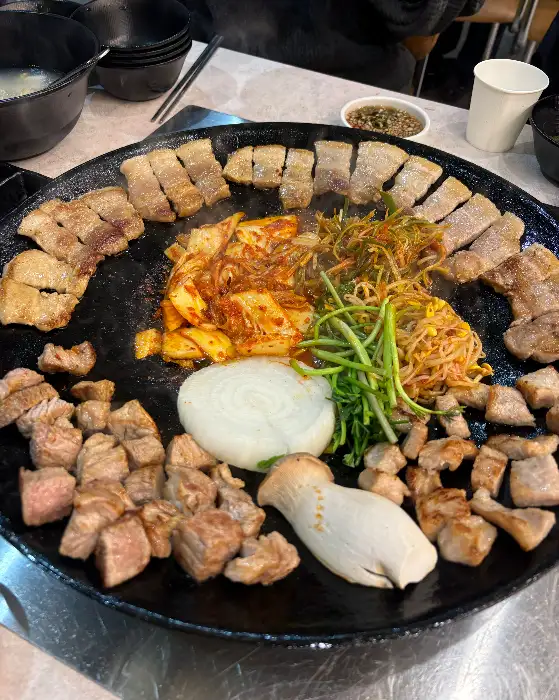 솥뚜껑 위에서 익어가고 있는 삼겹살과 볶음 채소들