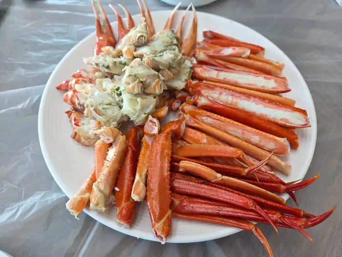 김이 모락모락 나는 찜기에서 갓 쪄낸 싱싱한 대게 한 상이 차려져 있습니다. 붉은빛이 도는 대게 다리와 몸통이 먹음직스럽게 놓여 있으며, 꽉 찬 살이 군침을 돌게 합니다.