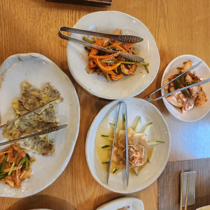 여러 가지 반찬이 담긴 접시들. 젓가락으로 음식을 집고 있다.