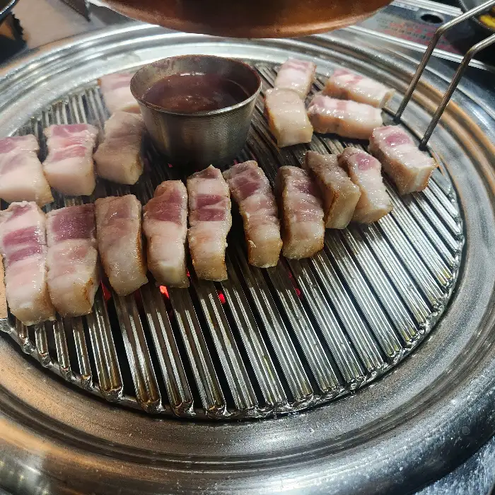 불판 위에서 노릇하게 구워지는 오겹살의 모습. 껍질 부분이 바삭하게 익어가고 있으며, 육즙이 풍부해 보이는 살코기 부분이 먹음직스럽습니다.