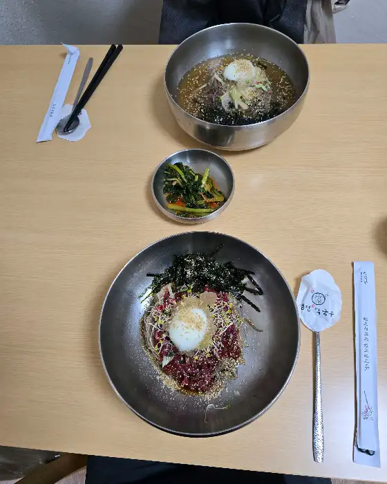 테이블 위에 놓인 두 개의 막국수 그릇과 곁들임 반찬
