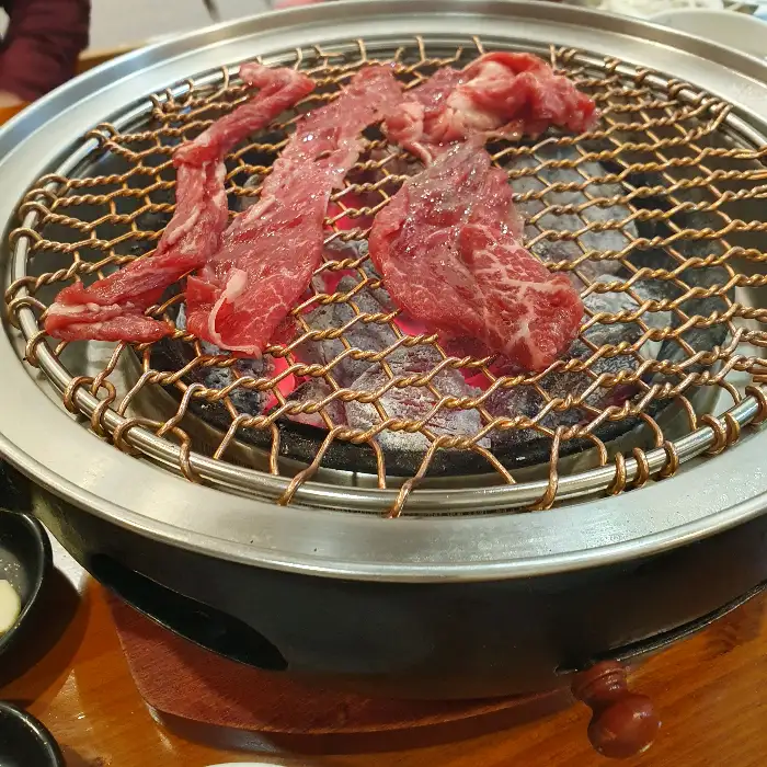 숯불 위에 올려진 얇게 썬 소고기. 붉은 살점과 불꽃이 먹음직스럽다.
