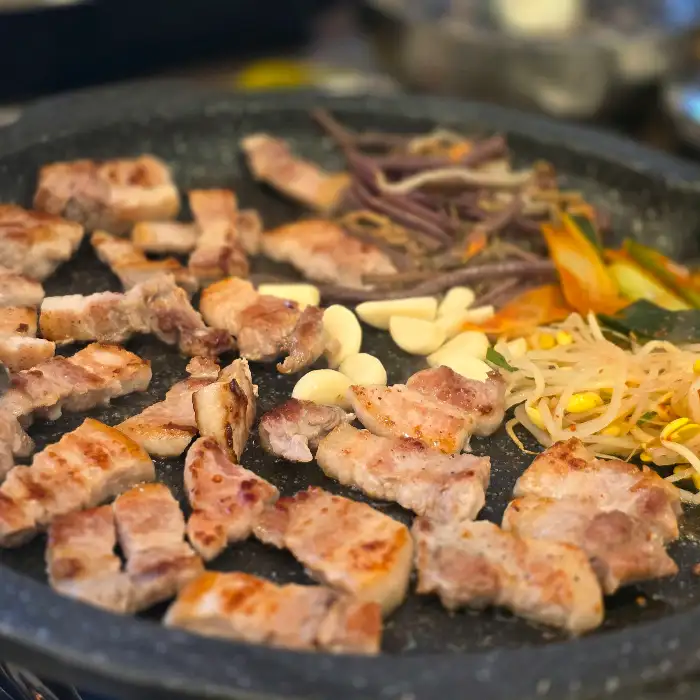 쌈 채소 위에 맛있게 구워진 삼겹살과 김치, 콩나물, 고사리 등이 올라가 있는 모습