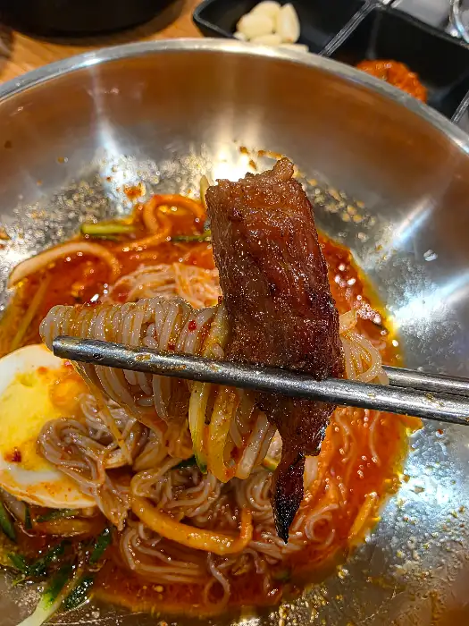 집게로 집어 올린 갈비 한 점을 냉면에 얹어 먹는 모습