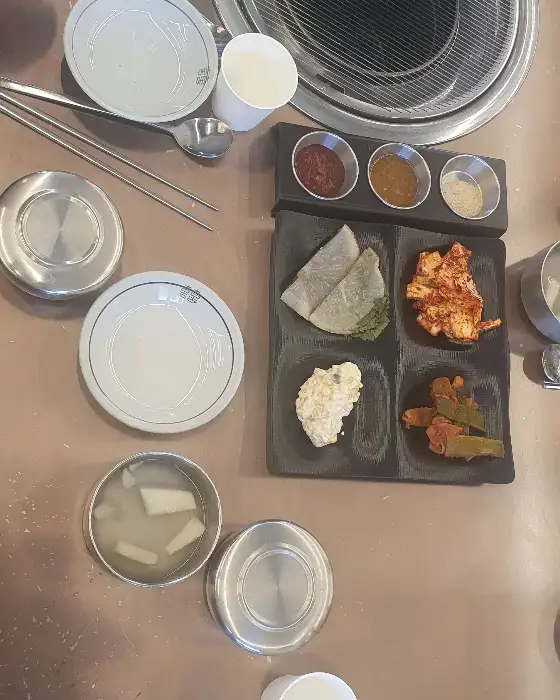 식탁 위에 정갈하게 차려진 밑반찬과 놋그릇 닭곰탕, 그리고 닭갈비가 담긴 접시
