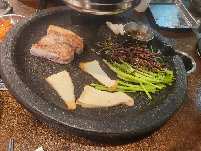불판 위에 구워지고 있는 삼겹살과 곁들임 채소