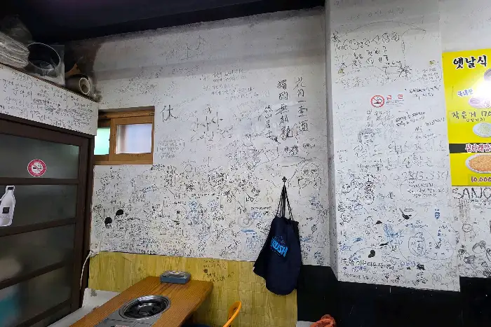 벽면에 빼곡하게 적힌 글씨들과 낡은 나무 테이블이 보인다.