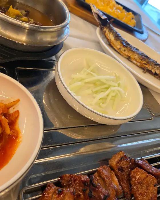 식탁 위에 놓인 샐러드와 밥, 그리고 숯불 위 고기의 일부