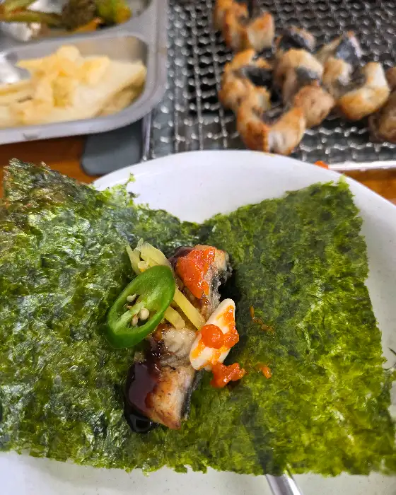 김 위에 장어, 깻잎 장아찌, 생강, 마늘 등을 올려 싸 먹는 모습