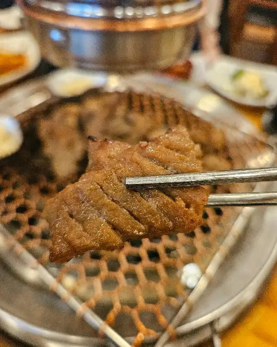 집게로 집은 잘 구워진 돼지갈비 조각