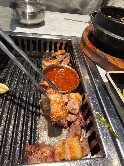 직원이 집게로 삼겹살 조각을 소스그릇에 찍어주고 있습니다.