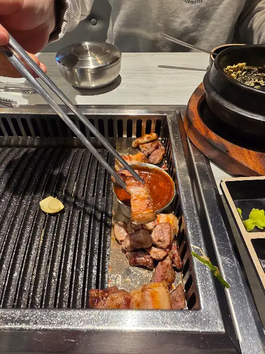 집게로 삼겹살을 소스에 찍어 그릇에 올리는 모습.