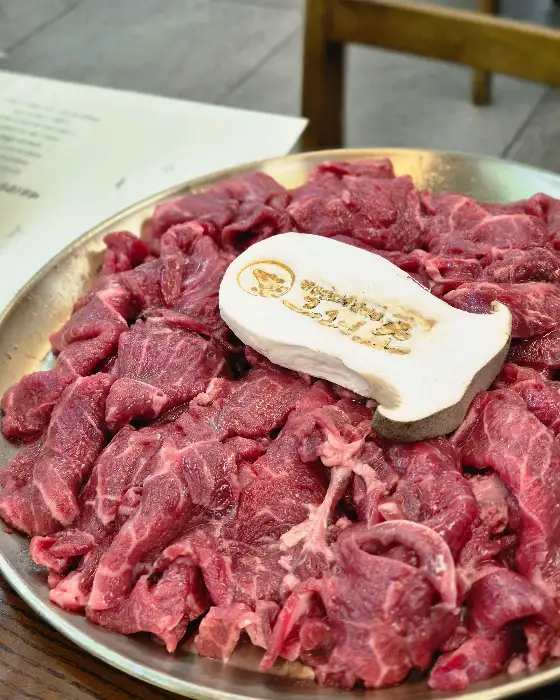 얇게 썬 소고기가 접시에 가득 담겨 있다. 중간에는 버섯이 놓여 있다.