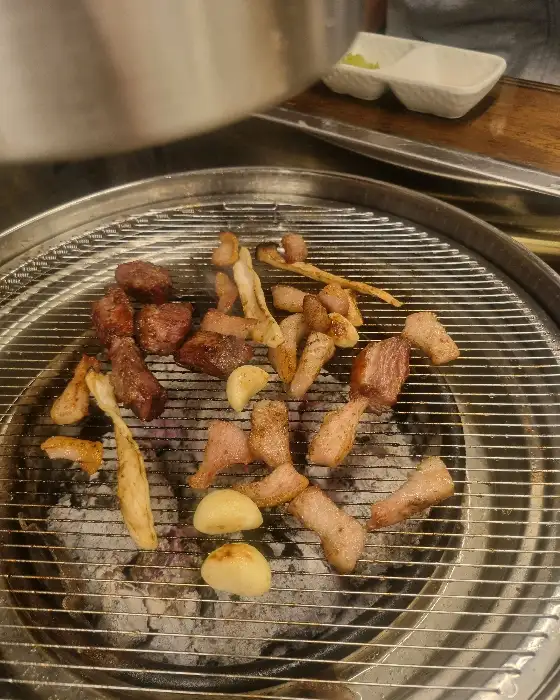 숯불 위에서 익어가고 있는 여러 조각의 고기와 마늘