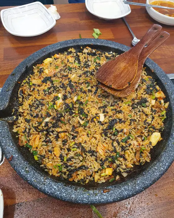 김이 모락모락 나는 볶음밥이 짙은 색의 돌판에 가득 담겨 있다.