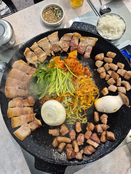 솥뚜껑 위에서 맛있게 익어가는 고기와 곁들임 채소들
