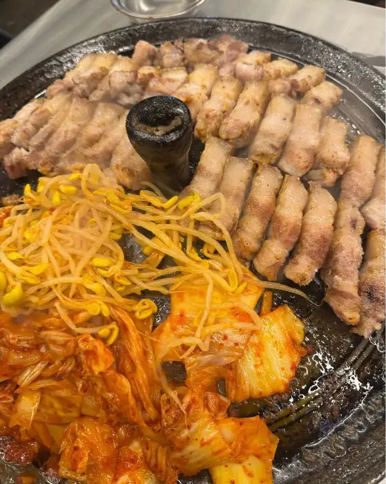 솥뚜껑 위에서 익어가는 삼겹살, 김치, 콩나물, 미나리