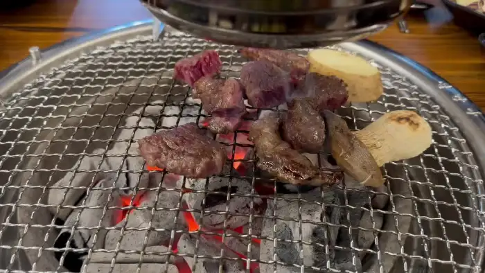 숯불 위에서 여러 조각의 고기와 버섯, 감자가 익어가는 모습