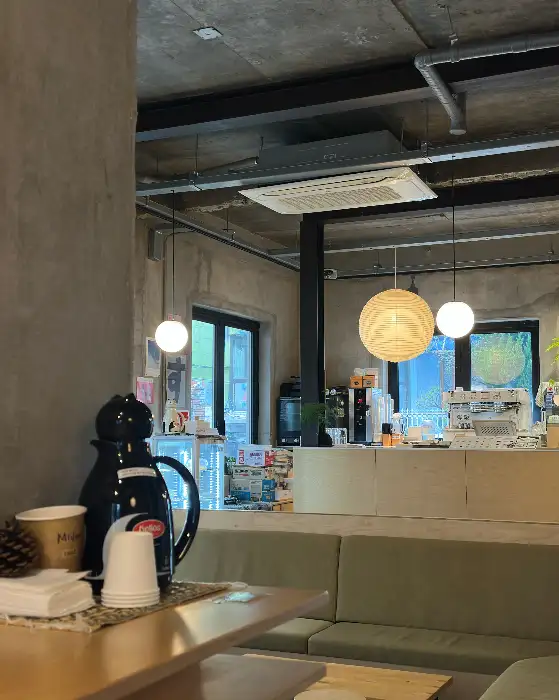카페 내부의 모습. 콘크리트 천장과 벽, 그리고 갓등 조명들이 보인다. 녹색 소파와 나무 테이블이 놓여 있다.