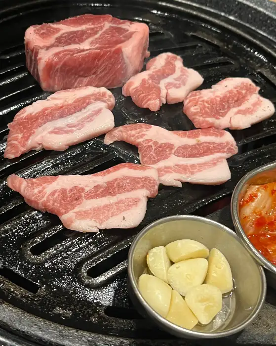 두툼한 삼겹살과 목살이 불판 위에 올라가 익어가고 있습니다. 신선한 고기의 육질이 살아있는 모습입니다.