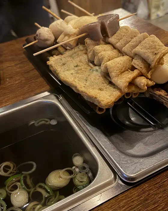 다양한 모양의 어묵이 꼬치에 꽂혀 나무 트레이에 담겨 있고, 옆에는 어묵 국물이 담긴 솥이 놓여 있는 모습