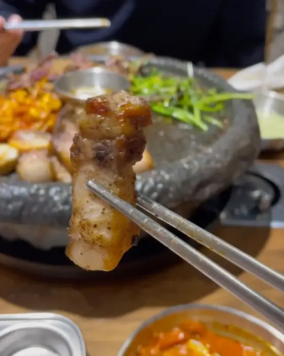 잘 구워진 삼겹살 한 점을 집게로 집어 올린 모습