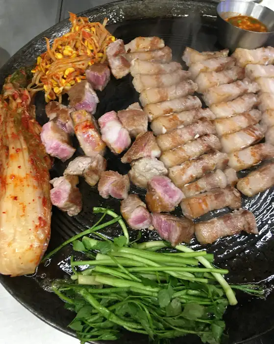 솥뚜껑 위 삼겹살, 김치, 콩나물, 미나리 모습