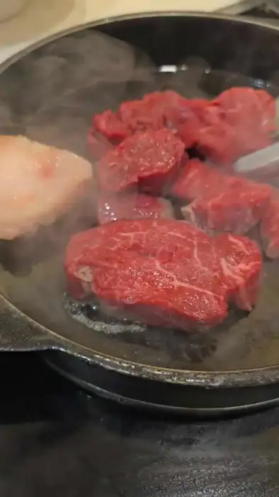 고기가 팬에서 익어가며 김이 피어오르는 모습. 직원으로 보이는 사람이 집게를 들고 고기를 뒤집고 있다.