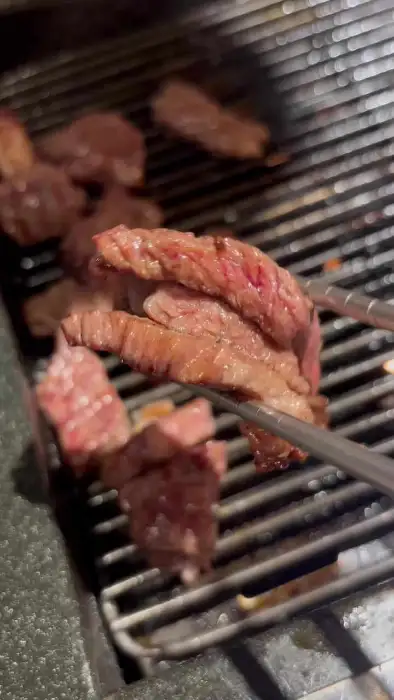 집게로 불판 위 소고기 조각들을 집어 올리고 있습니다.