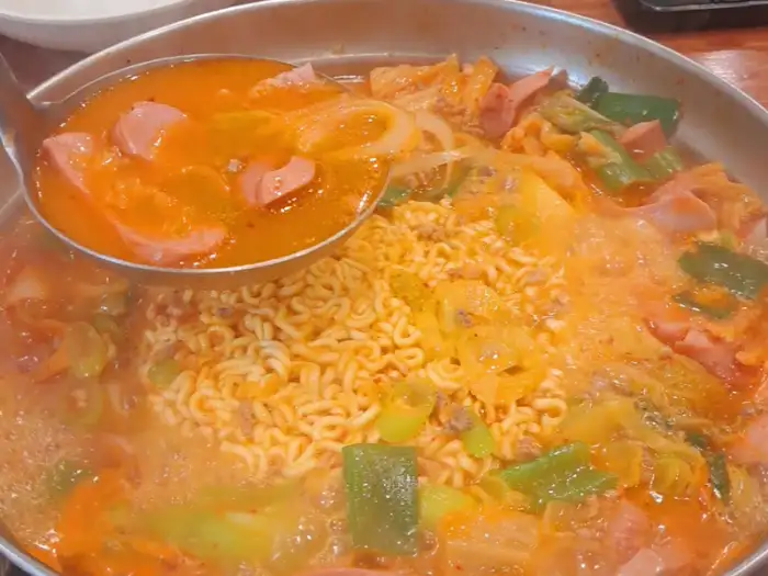 끓고 있는 부대찌개 냄비 클로즈업, 라면 사리와 햄, 야채 등이 보인다