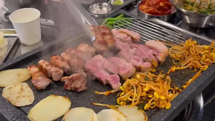 불판 위에서 지글지글 익고 있는 다양한 부위의 고기와 곁들임 채소
