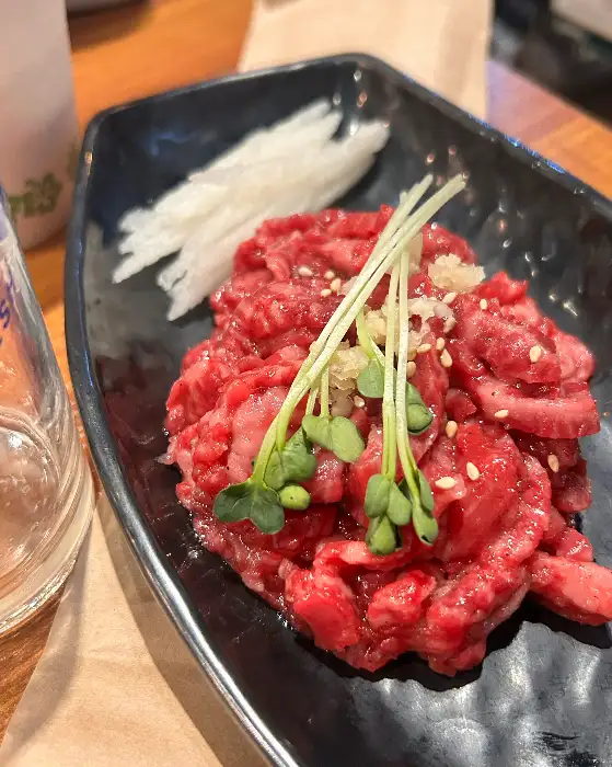 검은 그릇에 담긴 먹음직스러운 육회가 신선한 채소와 함께 올려져 있습니다.