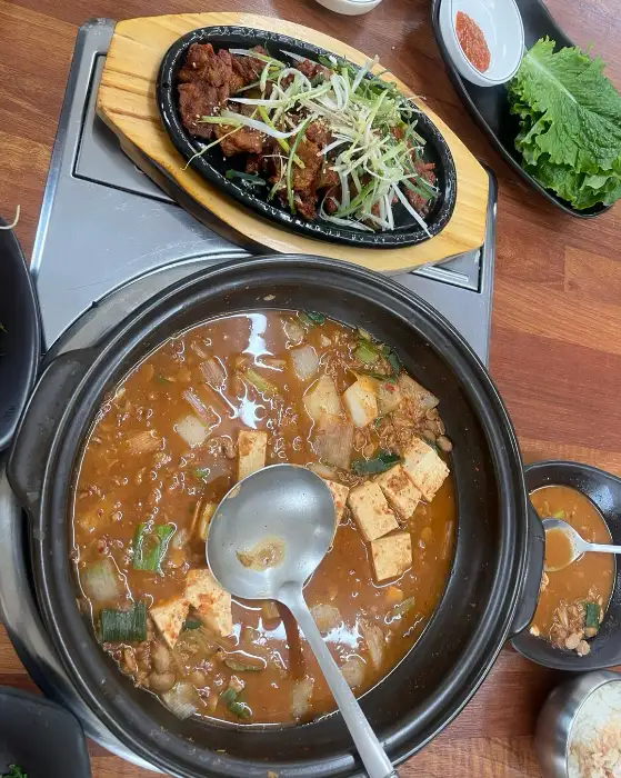 김이 모락모락 나는 청국장 전골과 초벌구이 된 삼겹살이 함께 나온 모습