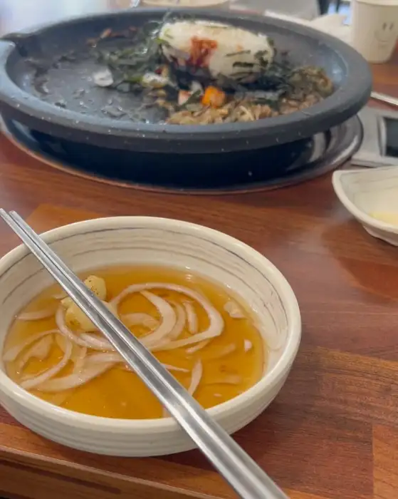 앞접시에 담긴 맑은 국물에 얇게 썬 양파가 띄워져 있고, 금속 젓가락이 놓여 있다.