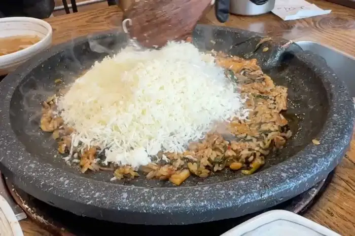 테이블에 놓인 둥근 돌판 위에서 오리불고기가 익어가는 모습, 그 위에 듬뿍 쌓인 치즈가 녹아내릴 준비를 하고 있다.
