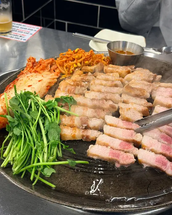 솥뚜껑 삼겹살을 집게로 집는 모습