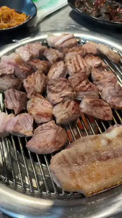 잘 구워진 흑돼지 조각들이 숯불 위에서 먹음직스럽게 익어가고 있다.