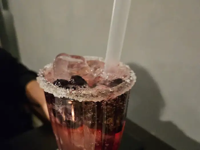 테두리에 설탕이 묻혀진 컵에 담긴 붉은색 음료수와 얼음, 베리류