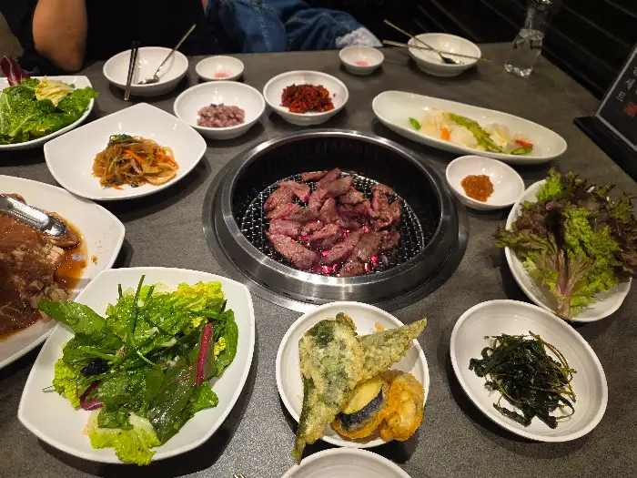 다양한 밑반찬과 함께 숯불에 구워지고 있는 고기, 그리고 신선한 쌈 채소